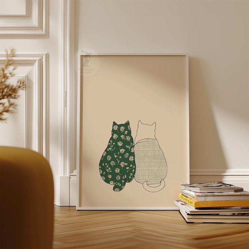 Puede incluir: Una impresi&oacute;n art&iacute;stica enmarcada con dos gatos estilizados. Uno de los gatos tiene un estampado floral verde oscuro, mientras que el otro tiene un dise&ntilde;o a cuadros marr&oacute;n claro. La obra de arte est&aacute; sobre un fondo beige, con una pila de libros en primer plano.