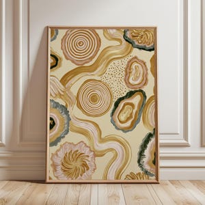 Puede incluir: Una impresión de arte mural rectangular que presenta un patrón abstracto de formas inspiradas en ágatas en tonos oro, beige y verde oscuro, círculos concéntricos y líneas onduladas fluidas sobre un fondo crema claro, dentro de un marco de madera.