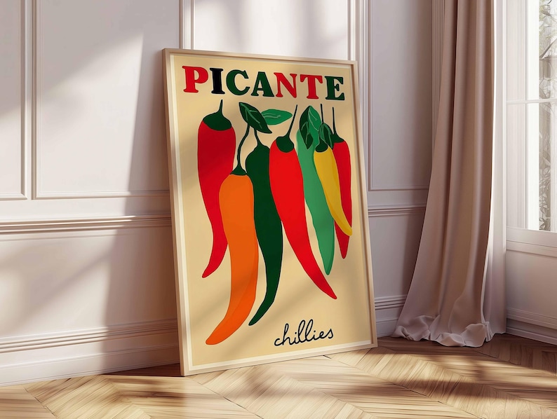 May include: A framed poster with the word "PICANTE" in red and green above a collection of stylized chili peppers in red, orange, green, and yellow. The word "chillies" is written in cursive at the bottom of the poster. The poster is leaning against a white wall.