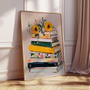 May include: A framed art print featuring a stack of books with a floral arrangement on top. The books are painted in various colors, including yellow, green, and floral patterns. The sunflowers and other flowers add a touch of nature to the artwork. The frame is a light wood color.
