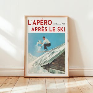 May include: A framed vintage poster with the text "L'APÉRO APRÈS LE SKI" in red. The poster depicts a skier jumping off a snowy roof, holding a tray with drinks. The poster is in a wooden frame.
