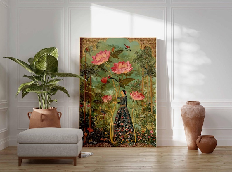 May include: A framed art print featuring a woman in a garden with large pink lotus flowers. The artwork has a vintage aesthetic with a green and gold color palette. A large potted plant and a gray ottoman are in the foreground.