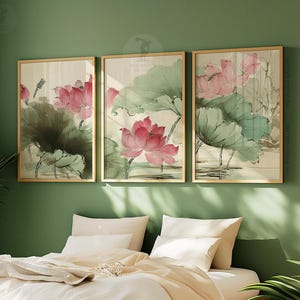 May include: Three framed art prints featuring watercolor paintings of pink lotus flowers and green leaves. The artwork is set against a neutral background, with gold frames. The prints are displayed on a green wall above a bed with white bedding.