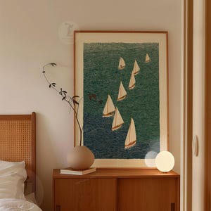 May include: A framed art print featuring a nautical scene with several sailboats on a textured teal-green sea. The artwork is displayed above a wooden cabinet, with a decorative vase and a small lamp.