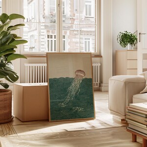May include: A framed art print featuring a jellyfish illustration. The artwork depicts a jellyfish with a brown bell and long, flowing tentacles in a teal ocean. The print is displayed in a light-filled room with a large window.