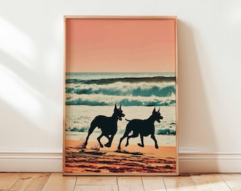 May include: Framed art print featuring two black dog silhouettes running on a beach. The artwork depicts a sunset with a pink sky and ocean waves. The print is displayed on a wooden floor.
