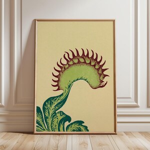 May include: A framed vertical art print featuring a stylised illustration of a Venus flytrap plant. The plant has a light green trap with dark red, spiky teeth and dark green, leafy foliage at the base, all set against a solid light beige background.