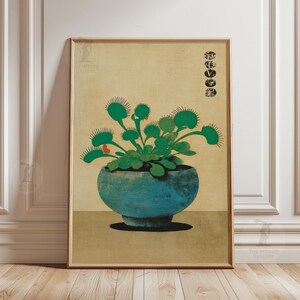 Op de afbeelding: Een ingelijste botanische prent met een Venusvliegenval in een blauwgroene pot. De plant heeft groene bladeren en rode accenten. De achtergrond is beige en de lijst is lichtbruin. Japanse tekst staat in de rechterbovenhoek.