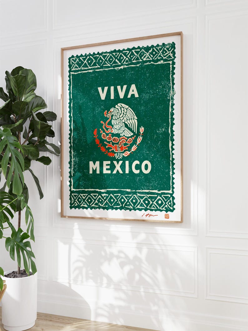 May include: Framed art print featuring the Mexican coat of arms and the words "VIVA MEXICO" in white on a green background. The print has a distressed, vintage look and is displayed on a white wall next to a potted plant.
