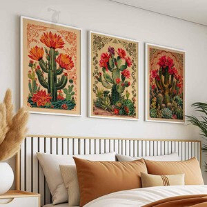 May include: Three framed vintage botanical prints featuring illustrations of red and green cacti with flowers. The prints are displayed on a white wall above a brown headboard with a white and brown bed.