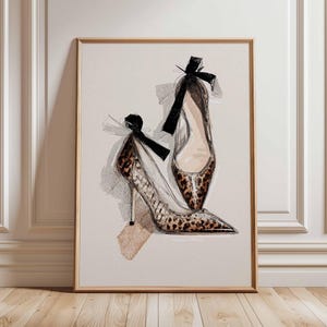 Op de afbeelding: Een artistieke print van twee hoge hakken. De schoenen hebben een luipaardprint, spitse tenen en dunne hakken. Elke schoen heeft een zwarte strik bij de hiel. Het kunstwerk is ingelijst in een lichtgekleurde houten lijst.