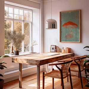 May include: A light-filled room with a wooden desk and two chairs. A framed mushroom print hangs on the wall. A large window offers a view of trees. A silver pendant light hangs above the desk. Plants and decor add to the room's aesthetic.