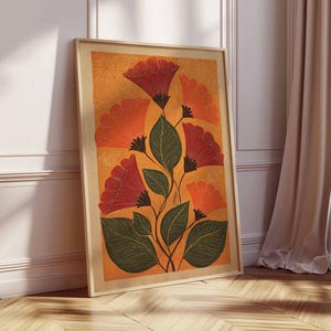May include: A framed floral art print featuring stylized red and orange flowers with green leaves against an orange background. The artwork is in a light wooden frame and leans against a white wall and wooden floor.