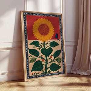 May include: A framed art print featuring a large yellow sunflower with a brown center, green leaves, and a blue bird. The artwork has a red and beige background with a blue border. The print is displayed on a wooden floor.
