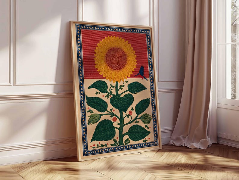 May include: A framed art print featuring a large yellow sunflower with a brown center, green leaves, and a blue bird. The artwork has a red and beige background with a blue border. The print is displayed on a wooden floor.