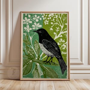 Może przedstawiać: Oprawiony wydruk artystyczny przedstawiający czarnego ptaka siedzącego na gałęzi z zielonymi liśćmi i białymi kwiatami. Tło podzielone jest na dwie zielone sekcje, z jasną drewnianą ramą. Grafika ma styl vintage, botaniczny.