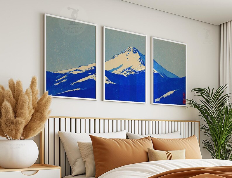 K&ouml;nnte beinhalten: Drei gerahmte Kunstdrucke, die eine Bergkette in Blau- und Wei&szlig;t&ouml;nen zeigen. Das Kunstwerk hat einen minimalistischen Stil mit hellblauem Himmel und wei&szlig;en R&auml;ndern. Die Drucke werden &uuml;ber einem Bett mit orangefarbenen Kissen angezeigt.