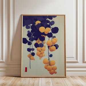 Op de afbeelding: Een ingelijste kunstdruk met een gestileerde illustratie van hangende gele vruchten en donkerblauwe bladeren tegen een lichtgroene achtergrond. Het kunstwerk heeft een minimalistische esthetiek met een rood rechthoekig accent linksonder.