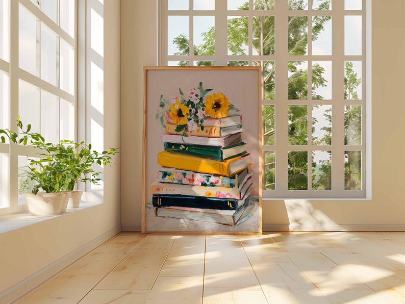 May include: A framed art print featuring a stack of books with a floral arrangement of sunflowers and other flowers on top. The books are various colors, including yellow, green, and floral patterns. The artwork is displayed in a room with a window and plants.