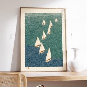 May include: A framed print featuring a stylized depiction of sailboats on a textured ocean. The artwork uses shades of blue and green to represent the water, with white sails catching the wind. The print is displayed on a wooden shelf with a white vase.