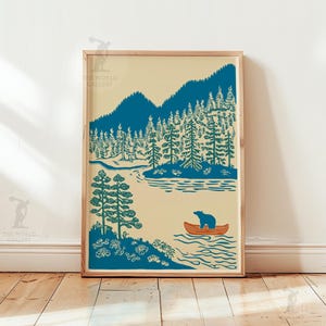 May include: A framed art print featuring a serene landscape with a teal forest, mountains, and a river. A bear is in an orange canoe. The artwork has a vintage aesthetic, with a cream-colored background and a wooden frame.