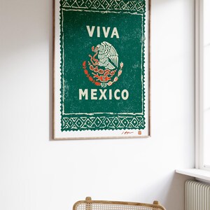 May include: A framed print with a green background and the words "VIVA MEXICO" in white. The print features the Mexican coat of arms, an eagle with a snake. The frame is a light brown color.
