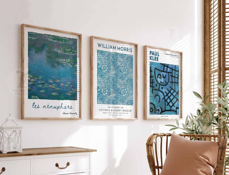 May include: Three framed art prints with wooden frames displayed on a white wall. The prints showcase artwork by Claude Monet, William Morris, and Paul Klee. The Monet print depicts water lilies, the Morris print has a blue floral pattern, and the Klee print has a blue abstract design.