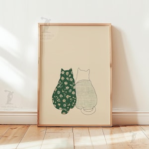 Puede incluir: Una impresi&oacute;n art&iacute;stica enmarcada con dos gatos estilizados. Uno tiene un estampado floral verde oscuro, el otro un estampado a cuadros gris claro. Los gatos est&aacute;n sentados juntos, de espaldas al espectador, sobre un fondo crema.