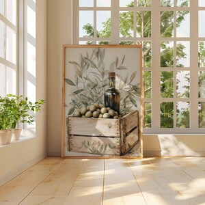 May include: A framed print featuring a still life with olives, a bottle, and olive branches. The olives are in a wooden crate. The artwork is displayed in a bright room with a window and plants.