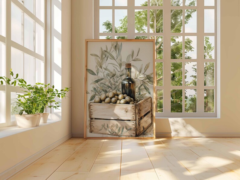 May include: A framed print featuring a still life with olives, a bottle, and olive branches. The olives are in a wooden crate. The artwork is displayed in a bright room with a window and plants.