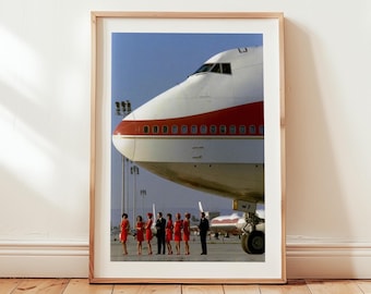 May include: A framed print featuring a Boeing 747 airplane with a red and white color scheme. A group of people in red dresses and black suits stand in front of the plane. The image is set against a clear blue sky.