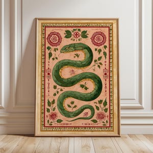 May include: A framed art print depicting a green snake with a yellow underbelly on a pink backdrop. The artwork incorporates floral and leaf patterns, framed by a decorative border. The frame is a warm gold colour.