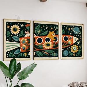 Könnte beinhalten: Ein Triptychon aus drei gerahmten Wandbildern mit Weltraummotiv. Die Illustrationen zeigen eine Rakete, die durch einen dunkelgrünen, sternenklaren Himmel fliegt, verziert mit Sonnenblumen, Blattwerk, einem weißen Hasen und einem braunen Bären.