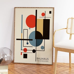 May include: A framed Bauhaus art print with a cream background, displaying geometric shapes in red, black, blue, and yellow. The print includes the text "BAUHAUS 1924 DAS MUSEUM FUR MODERNE KUNST UND SKULPTUR BERLIN". The frame is light brown.