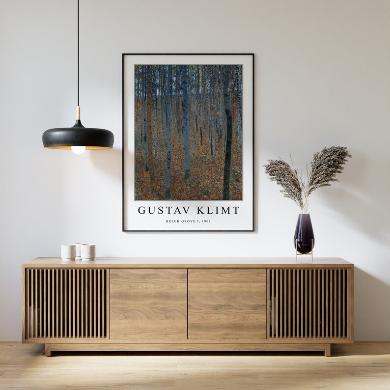 May include: A framed print of Gustav Klimt's "Beech Grove I" painting, featuring a stylized depiction of a forest with tall trees and a patterned ground. The print is displayed on a wooden cabinet with a light wood finish.