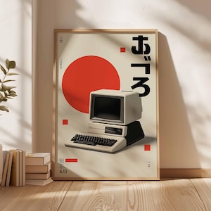 Puede incluir: Un p&oacute;ster enmarcado con un dise&ntilde;o de ordenador retro. El p&oacute;ster tiene un fondo beige con un gran c&iacute;rculo rojo y texto japon&eacute;s. El ordenador es de color blanco roto con un teclado negro. El p&oacute;ster est&aacute; en un marco de madera.