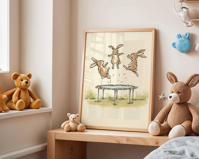 May include: A framed illustration depicts three brown rabbits jumping on a trampoline. The artwork is set against a light background, with a wooden frame. The scene is reminiscent of a children's book illustration, with a playful and whimsical theme.
