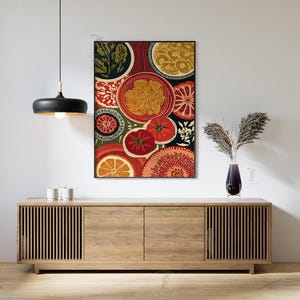 May include: A framed art print featuring a colorful still life of food items. The artwork includes images of tomatoes, oranges, pasta, and decorative patterns in shades of red, orange, green, and yellow. The print hangs above a wooden cabinet.
