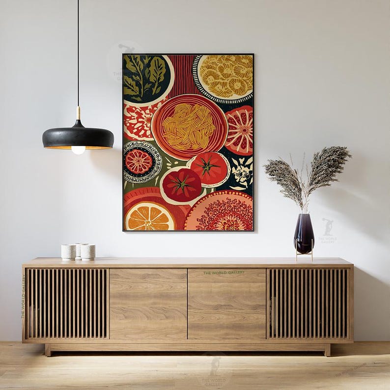 May include: A framed art print featuring a colorful still life of food items. The artwork includes images of tomatoes, oranges, pasta, and decorative patterns in shades of red, orange, green, and yellow. The print hangs above a wooden cabinet.