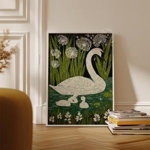 May include: A framed art print featuring a white swan with two cygnets swimming in a pond. The artwork has a black background with green reeds and white flowers. The print is displayed on a wooden floor.