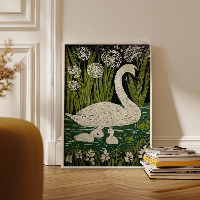 May include: A framed art print featuring a white swan with two cygnets swimming in a pond. The artwork has a black background with green reeds and white flowers. The print is displayed on a wooden floor.