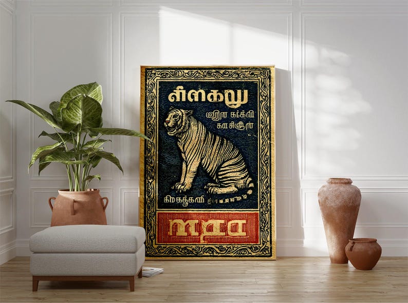 May include: A framed artwork featuring a tiger illustration in gold against a dark blue background. The artwork includes text in a foreign language and is framed with a gold border. The artwork is displayed in a room with a plant, ottoman, and decorative vases.