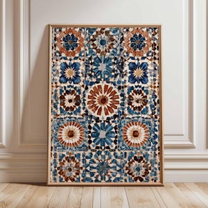 May include: Framed art print with a repeating pattern of geometric floral designs in blue, brown, and white. The artwork is displayed in a light brown wooden frame. The print is a decorative element, adding a touch of warmth to the room.