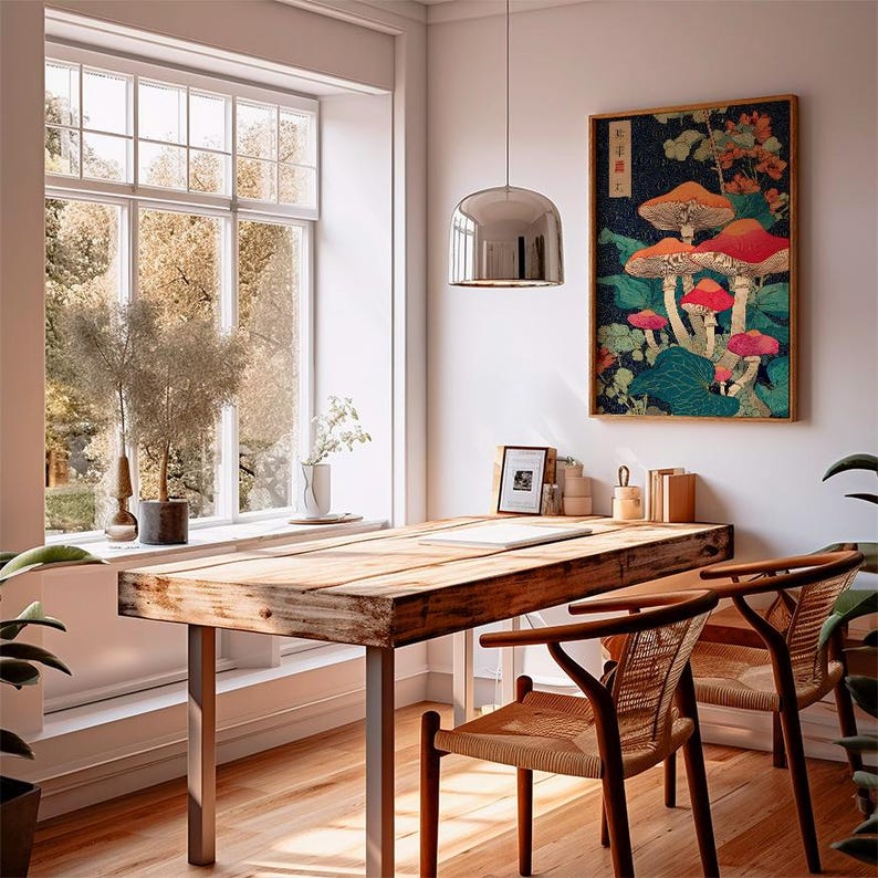 May include: A dining room scene with a wooden table and metal legs, two woven chairs, and a framed mushroom artwork. A large window offers a view of trees. A silver pendant light hangs above the table, and plants add greenery.