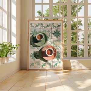May include: A framed artwork featuring two cups of coffee on saucers, one green and one coral, set against a backdrop of decorative tiles. The artwork is displayed in a sunlit room with a window and potted plants.