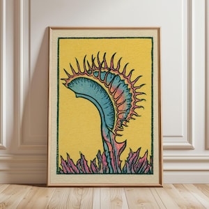 May include: A framed art print featuring a stylized illustration of a Venus flytrap plant. The plant has a blue-green trap with pink-tipped teeth, set against a solid yellow background. The base of the plant shows pink and green foliage.