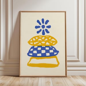 May include: A framed wall art print on a cream background featuring a stacked illustration. The design includes a blue flower at the top, a yellow patterned cushion, a blue and white checkered cushion, and a yellow rectangular base.