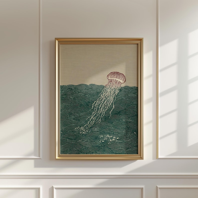 May include: Framed art print featuring a jellyfish illustration. The artwork depicts a jellyfish with a red bell and long, flowing tentacles in a teal ocean. The print is in a gold frame and hangs on a white wall.