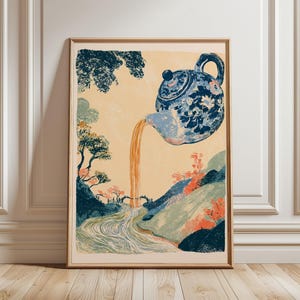 Può includere: Una stampa artistica incorniciata raffigurante una teiera con motivi floreali blu e bianchi che versa un liquido arancione in un fiume che scorre attraverso un paesaggio di alberi verde scuro, colline e un piccolo ponte su sfondo crema.