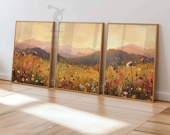 May include: Three framed landscape paintings with a field of wildflowers in the foreground and a mountain range in the background. The paintings are in a light wood frame and have a warm, earthy color palette.